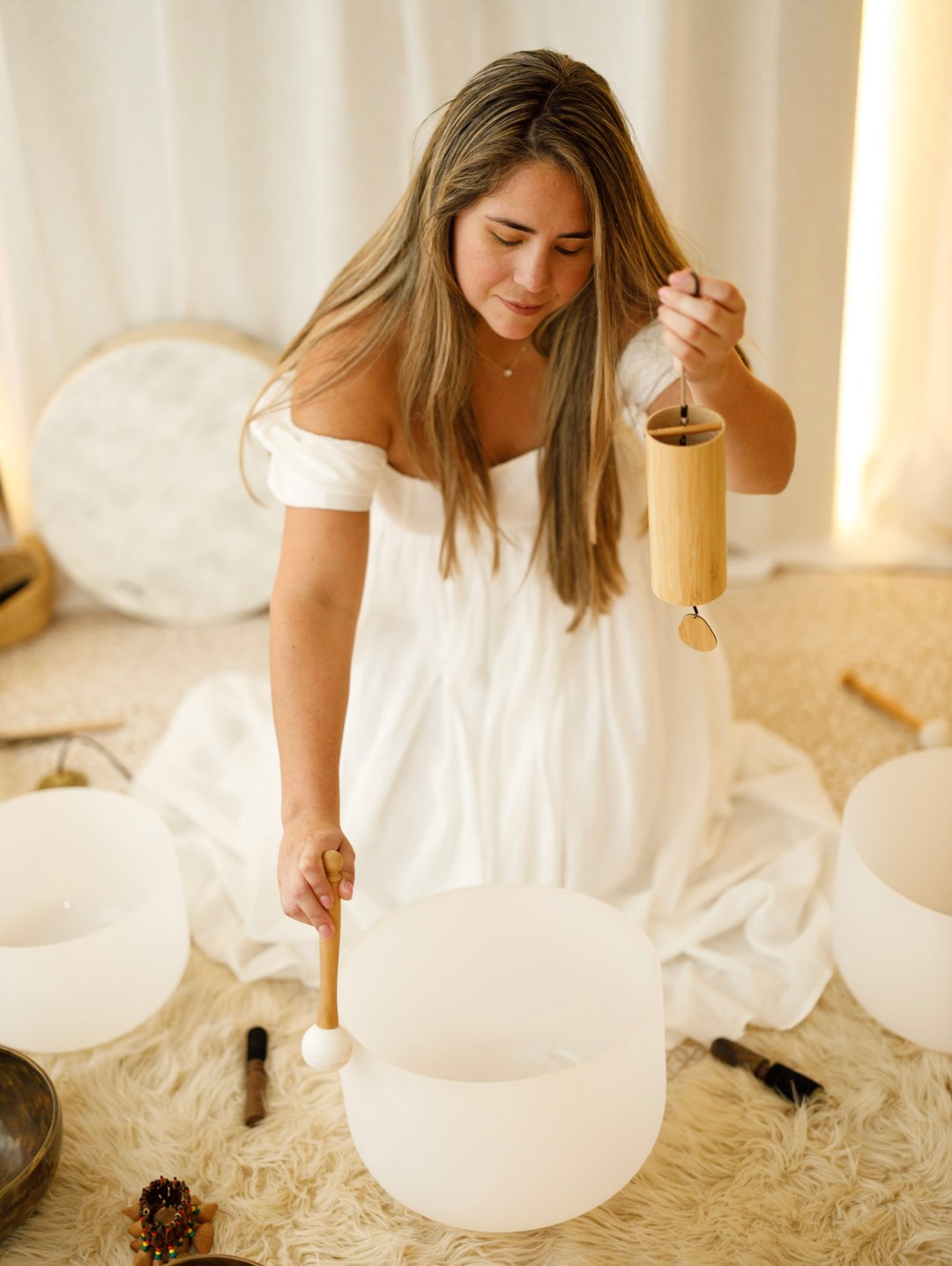 Celeste playing a crystal singing bowl with a bamboo chime in a warm sanctuary